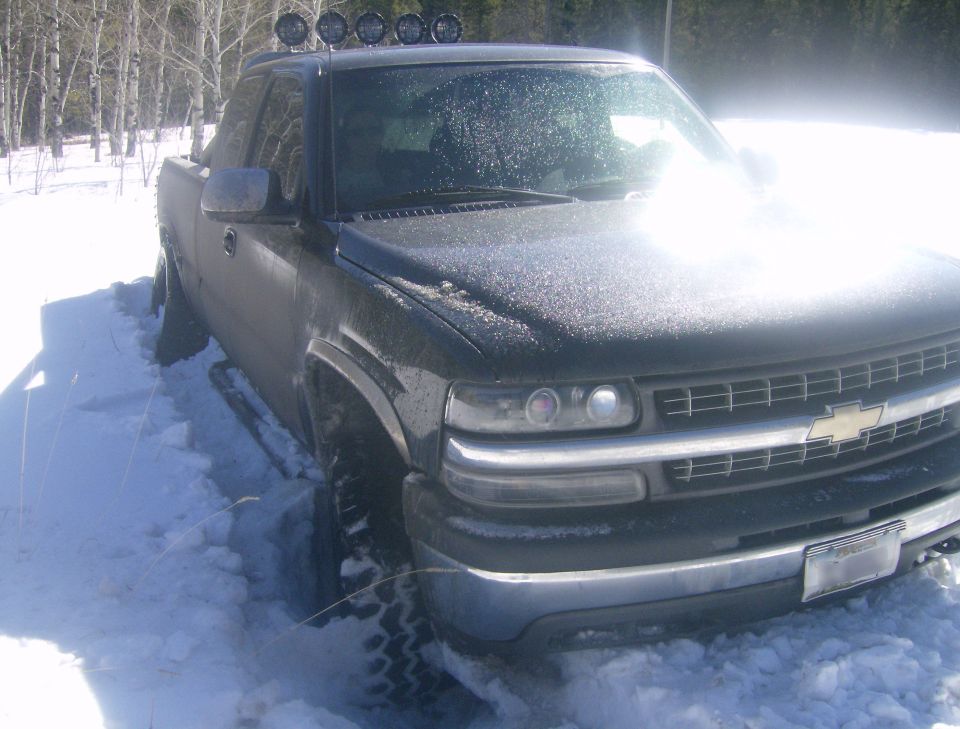 Dark pickup truck stuck in snow, with roof lights.