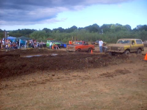 1976 Ford F-100 - Mud bog event with several trucks and spectators gathered on a cloudy day.