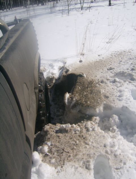 1990 Ford Bronco - A vehicle is stuck in a snow drift, with its tire partially submerged in mud and snow.