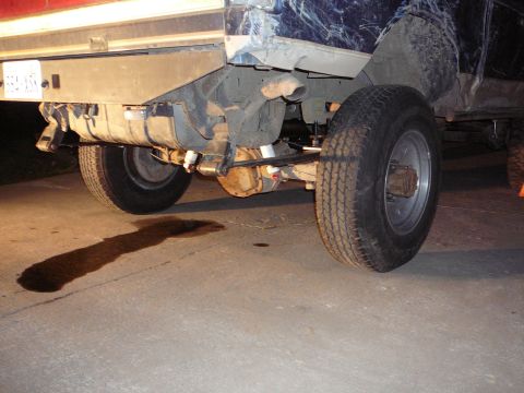 1991 Ford Bronco - The rear suspension and axle of a 1991 Ford Bronco are visible, with a fuel tank and an oil stain on the pavement.