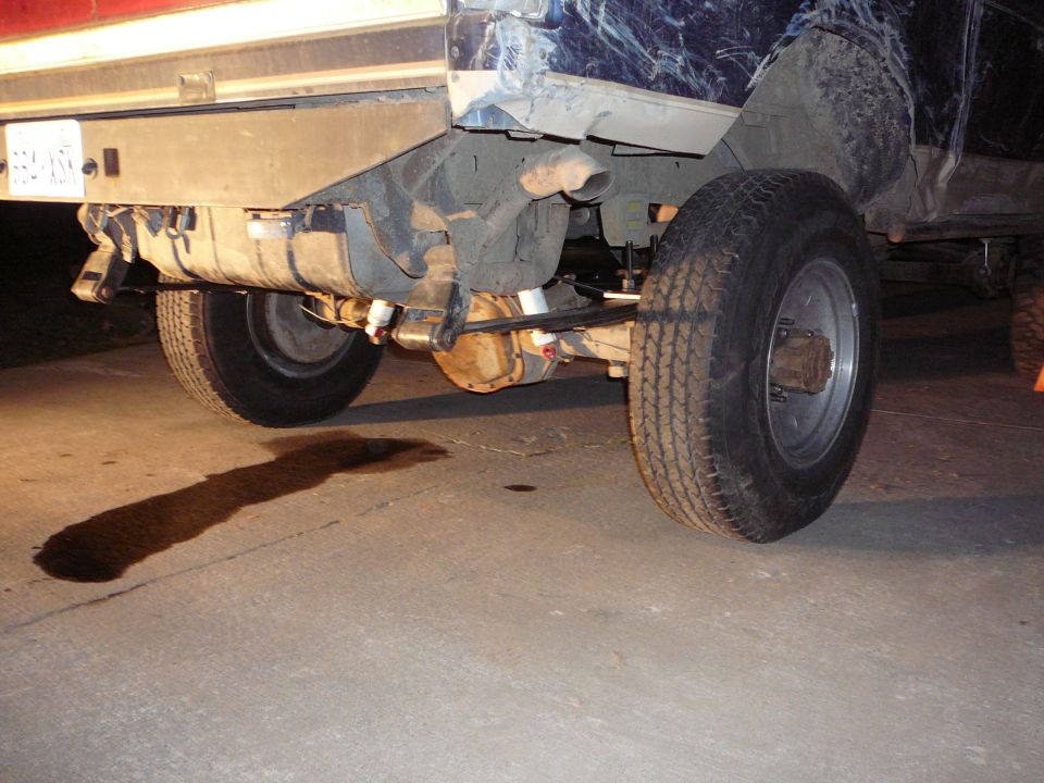1991 Ford Bronco rear axle with leaf springs, fuel tank, and a puddle of oil on the ground
