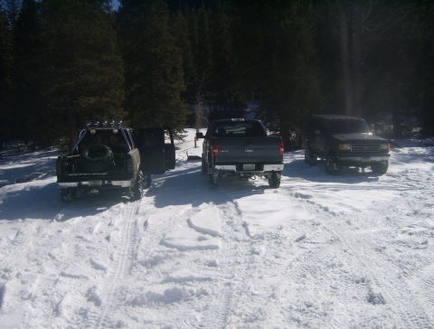 1990 Ford Bronco - Several trucks and SUVs are parked in a snowy area, with trees in the background.