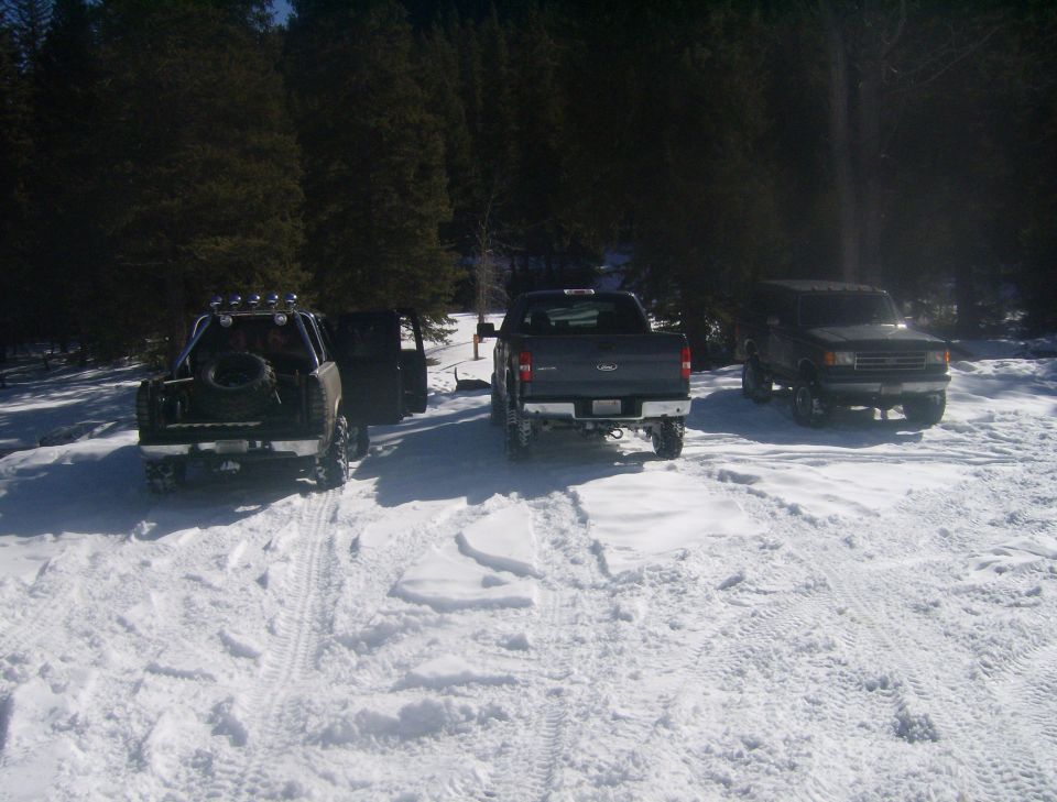 Three SUVs parked in snow. One is a Ford Bronco, another is a Ford pickup truck, and the third is a modified SUV with a spare tire on the back