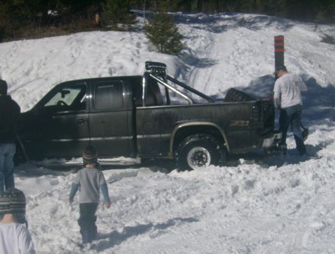 1990 Ford Bronco - A dark pickup truck is stuck in deep snow with people around it.