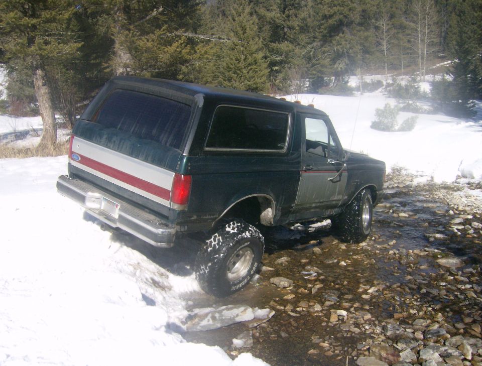 Dark green Ford Bronco with red and white stripe on rear, driving in snow and water