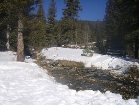 1990 Ford Bronco - A black SUV is parked on a snow-covered embankment beside a rocky stream.