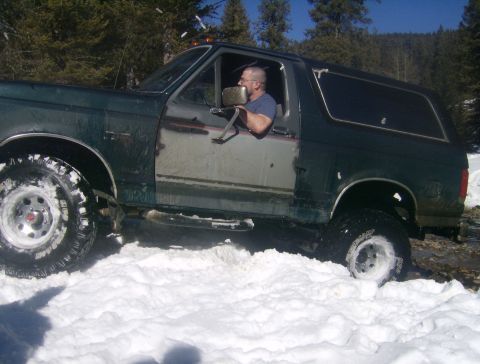 1990 Ford Bronco - A 1990 Ford Bronco navigates a snowy, off-road terrain with its driver behind the wheel.