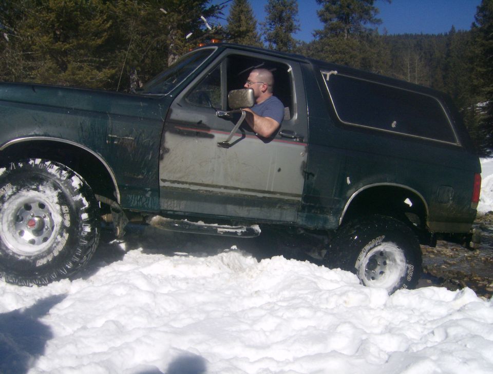 1990 Ford Bronco driving through deep snow, driver visible