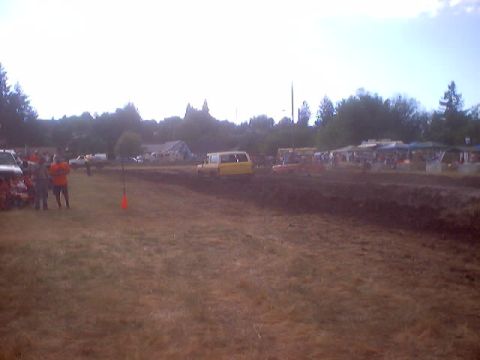 1976 Ford F-100 - A yellow van navigates a muddy course during an event with tents and people visible.