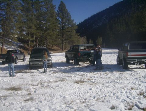 1990 Ford Bronco - Several SUVs and trucks are parked in a snowy, wooded area, with a 1990 Ford Bronco visible from the rear.