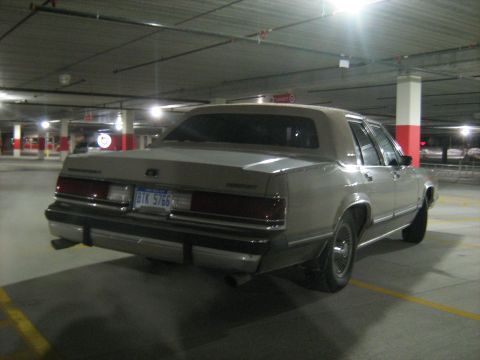 1988 Mercury Grand Marquis - A tan 1988 Mercury Grand Marquis sedan is parked in a concrete parking garage.
