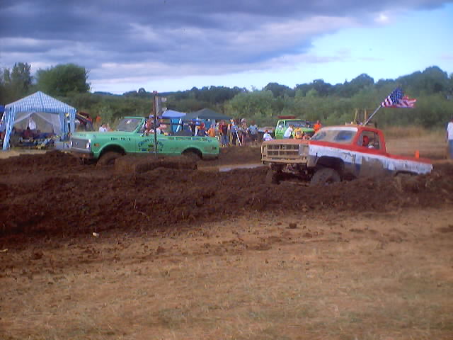 Red and white pickup truck stuck in mud, front view. American flag on antenna