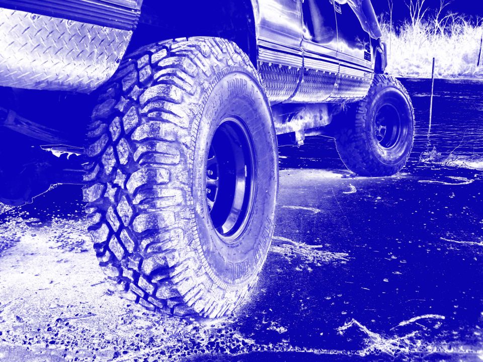 Close-up of large off-road tires on a truck, showing diamond plate fender and side body panel