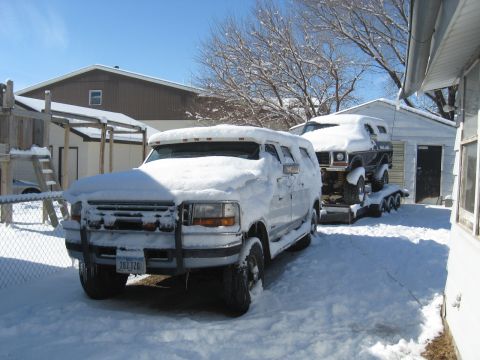 1978 Ford Bronco - A white van tows a trailer carrying a black SUV through a snowy yard.