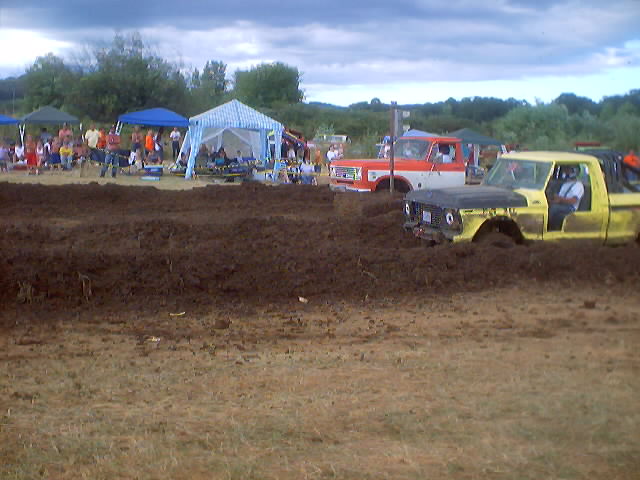 1976 Ford F-100 and an orange and white truck stuck in mud at a drag race