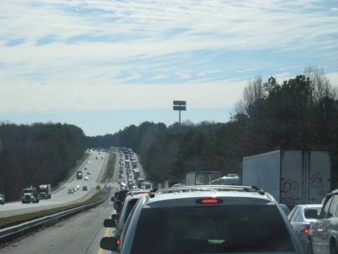 1978 Ford Bronco - A long line of vehicles are stuck in traffic on a highway, with trees lining the sides.
