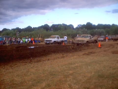 1976 Ford F-100 - Several trucks are gathered at a muddy outdoor event, with people watching and a bulldozer visible.