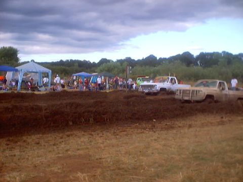 1976 Ford F-100 - Trucks compete in a mud drag race event with spectators gathered under tents.