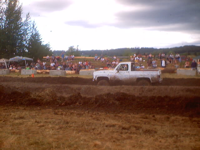 White pickup truck with mud tires driving through a mud pit