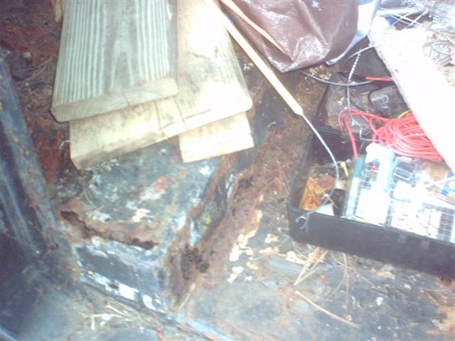 Interior of a rusty vehicle, showing floor rust and stored wood and wires