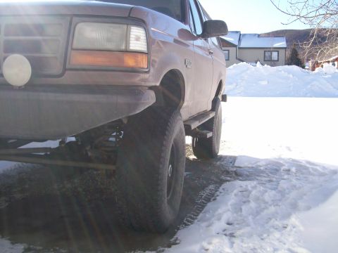 1993 Ford Bronco - A brown Ford Bronco sits parked in a snowy landscape, its large tires visible.