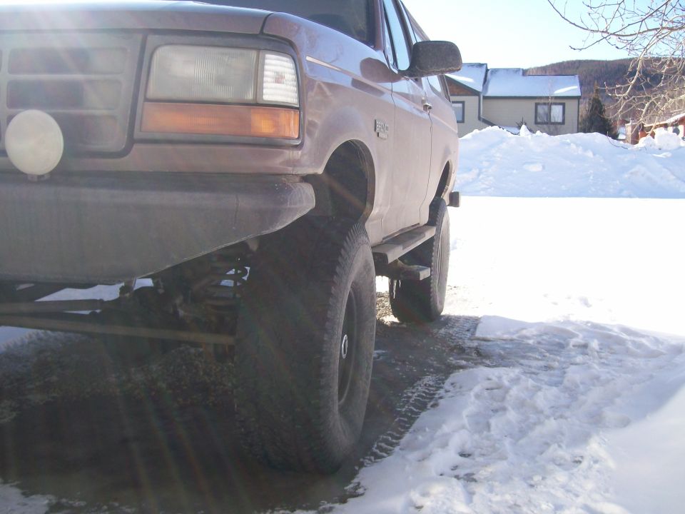 Low front 3/4 of lifted maroon Ford Bronco on snow showing front axle and lift