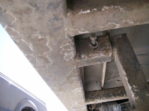 1993 Ford Bronco - Underside close-up of a truck frame rail and body mount, showing salt-crusted steel with a bolt through a bracket and a welded tube brace t…