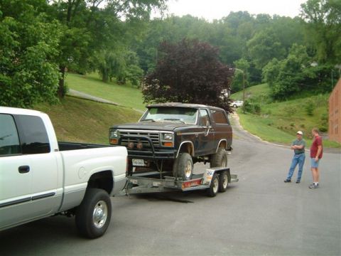 1982 Ford Bronco - A black Ford Bronco is being towed on a trailer by a white pickup truck, with two men standing nearby.