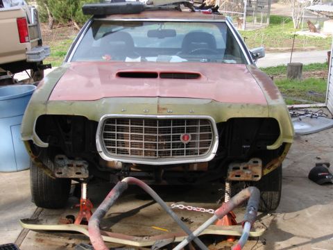 1973 Ford Ranchero - Front view of a 1970s Ford project car sitting on jack stands with the front bumper and headlight buckets removed, exposing the bumper brac…