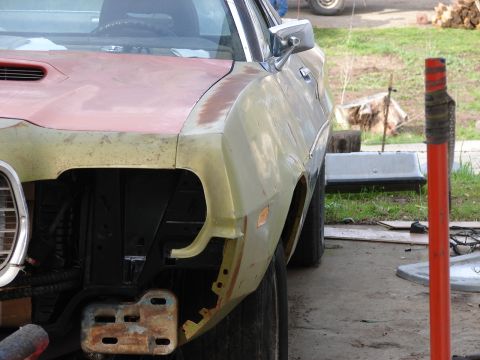 1973 Ford Ranchero - Driver-side front of a two-tone project car mid-bodywork, its nose in red primer and the fender and door in cream with surface rust, the fr…