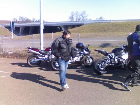 2008 Kawasaki Ninja R - A group of sport motorcycles are parked outdoors, with a man standing nearby. The scene includes a highway overpass in the background.