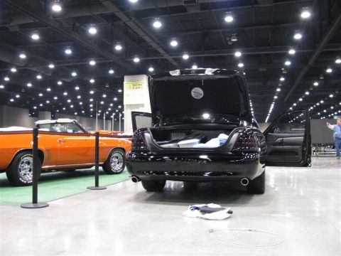 2003 Mercury Marauder - Two cars on display at a car show, one black sedan and one orange convertible.
