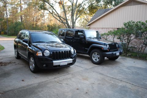 2008 Jeep Wrangler - Two black Jeep SUVs, a Wrangler and a Compass, are parked side-by-side in a concrete driveway.