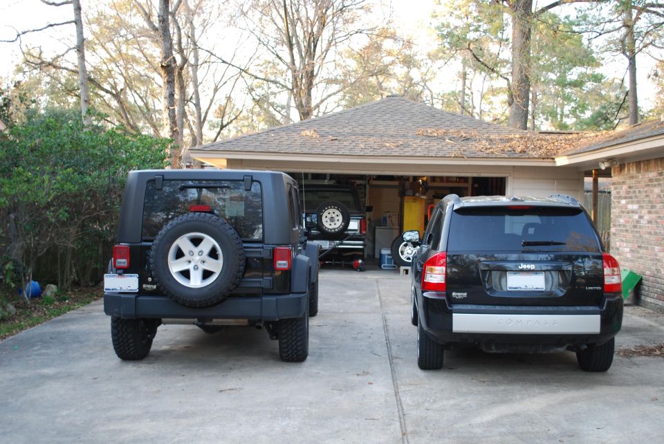 rear view of a black Jeep Wrangler and a black Jeep Compass parked in front of a garage