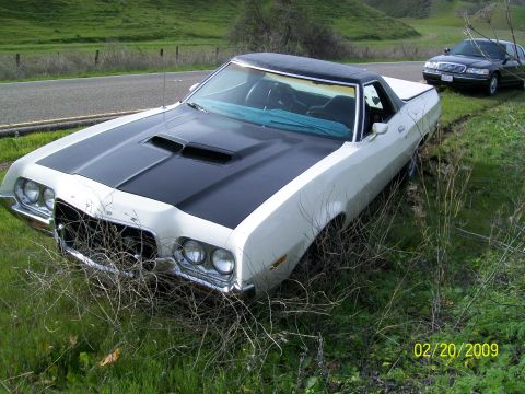 1972 Ford Ranchero - A white and black 1972 Ford Ranchero with a black hood scoop is parked off the side of the road, with a police car behind it.