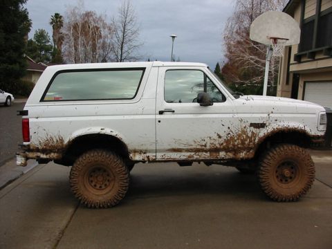 1996 Ford Bronco - Mud-splattered white Ford Bronco parked on a driveway under a cloudy sky.