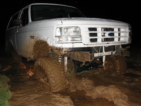 1996 Ford Bronco - This vehicle is stuck in a muddy off-road situation, with its tires submerged in thick mud.