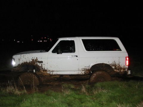 1996 Ford Bronco - White Ford Bronco navigates a muddy terrain at night, with its tires deep in the mire.