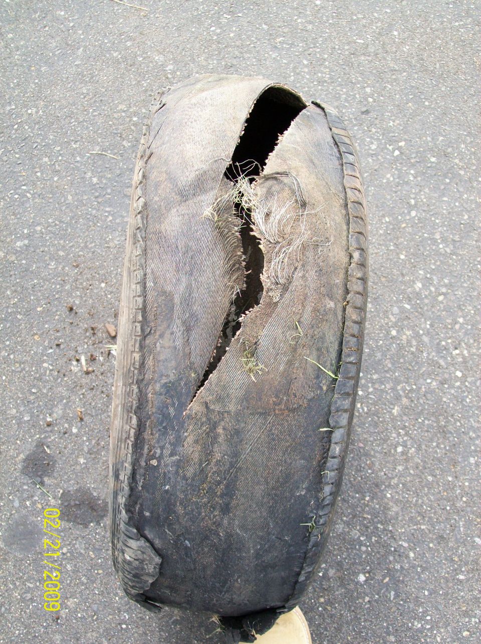 Worn tire with a large blowout tear lying on pavement