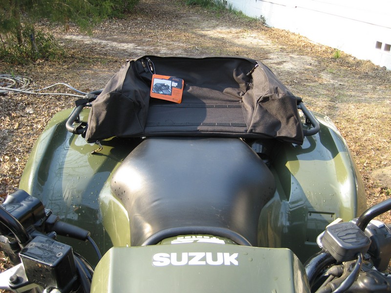 ATV's rear seat area with a black rack bag on top. An orange camera is inside the bag