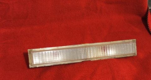 1989 Ford Bronco II - Clear plastic marker light assembly, likely for a vehicle, rests on a red textured surface.