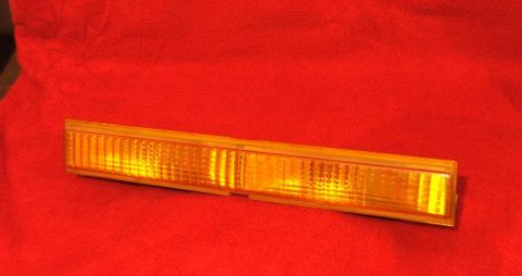 1989 Ford Bronco II - Amber turn signal lens with vertical fluting and a clear end section, on a red textured surface.