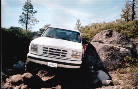 1996 Ford Bronco - White Ford truck with a distinctive grille is shown off-roading on a sunny day.