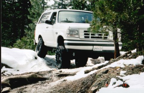 1996 Ford Bronco - A white 1996 Ford Bronco navigates a snowy, off-road path through a wooded area.