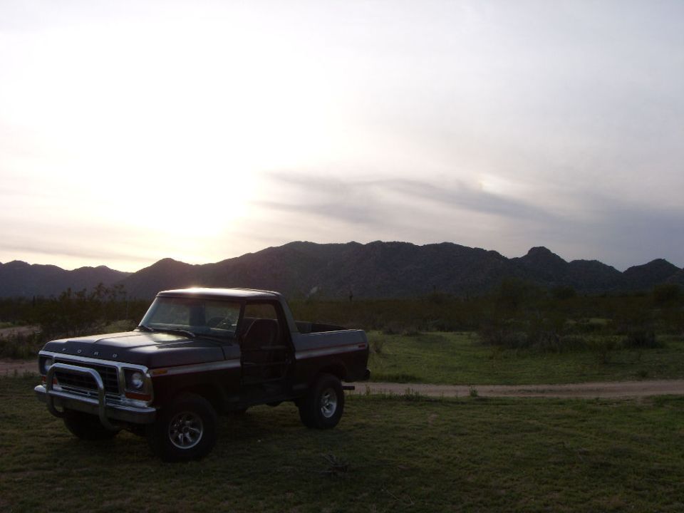 Topless dark Ford Bronco parked on desert grass at sunset with mountains behind