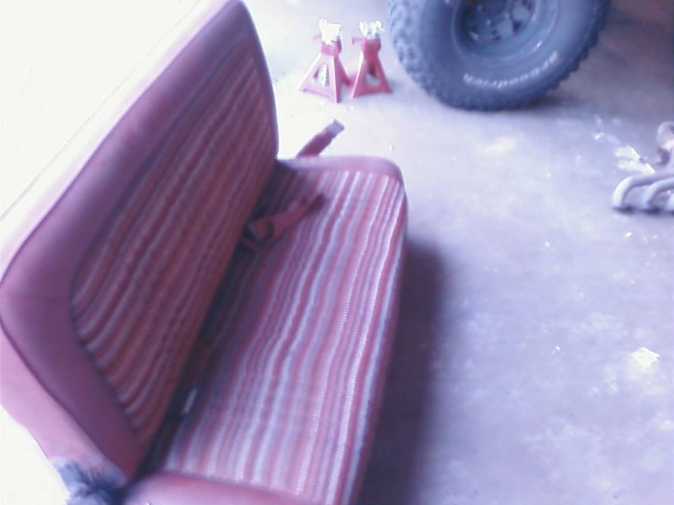 Red and white striped bench seat with seatbelt, tire and jack stands in background.