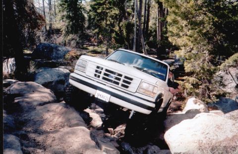 1996 Ford Bronco - This 1996 Ford Bronco is shown tackling a rocky trail with trees and boulders surrounding it.