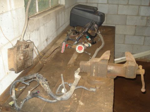 1991 Ford Bronco - A workbench in a basement setting with various automotive wiring harnesses and a vise. A wooden electrical box is mounted on the wall.
