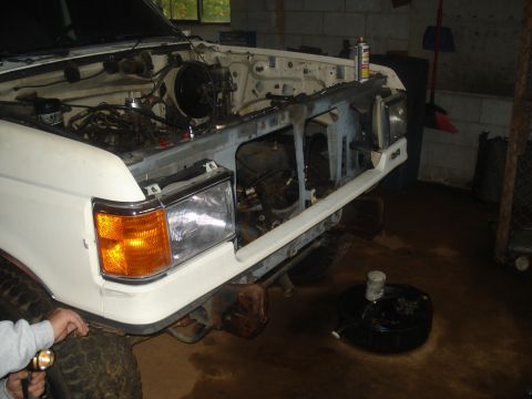 1991 Ford Bronco - The front end of a white 1991 Ford Bronco is shown with the hood open, revealing the engine compartment. The vehicle is in what appears to…