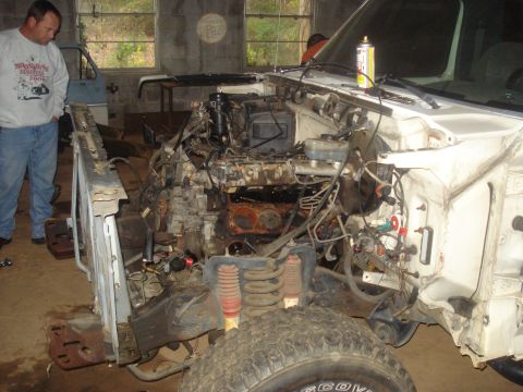 1991 Ford Bronco - A man in a sweatshirt and jeans stands next to the disassembled engine bay of a white Ford truck, possibly a Bronco, in a garage. The front…